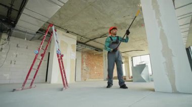 Duvarları ve sütunları bitirilmemiş binaların iç kısımlarına asan profesyonel ressam yenileme çalışmaları sırasında güvenlik kaskı takarken boya silindirleriyle yüzeyleri hazırlıyor.