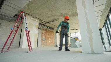 Güvenlik üniforması giyen profesyonel müteahhit paten fırçası kullanarak duvarları asıyor, tamamlanmamış inşaat sahasında ustalıklı yenileme teknikleriyle düzenli olarak çalışıyor.