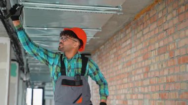 Profesyonel elektrikçi elektrik tesisatı üzerinde çalışıyor ve inşaat halindeki bir binaya askıya alınmış tavan panelleri yerleştiriyor, güvenlik ve işlevselliği sağlıyor