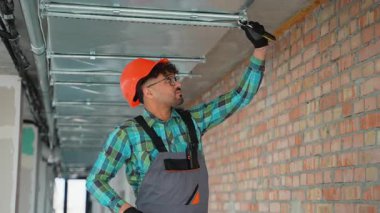 Profesyonel elektrikçi, ticari binanın tavan ızgarası içine elektrik kabloları ve ışıklar yerleştiriyor, etkin altyapı geliştirme sırasında kalifiye elektrik bakımını vurguluyor