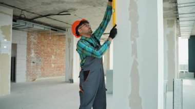 Üniforma giyen profesyonel müteahhit inşaat halindeki bir binanın içindeki duvarın dikey hizasını kontrol etmek için ruh seviyesini kullanır.