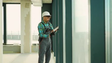 Üniforma giyen profesyonel müteahhit bitmemiş bir binanın duvarlarını dikkatlice inceleyerek kaliteyi ve yapısal bütünlüğü sağlama alıyor.