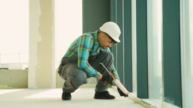 Profesyonel inşaat işçisi, inşaat halindeki modern bir binanın pencere çerçevesine hava geçirmez ve hava geçirmez kurulumunu sağlamak için dolgu macunu sıkıca yapıştırıyor.