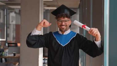 Sevinçli üniversite mezunu akademik regalia giyerek, diplomayı tutarken muzaffer bir şekilde kollarını kaldırarak ve başarılı bir eğitim yolculuğunun ardından gururla ışıldayarak mezun oldu.