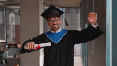 Mezuniyet elbisesi ve şapkası giyen genç mezun akademik başarısını kutluyor, diplomasını tutuyor ve neşe ve heyecan ifade ediyor.