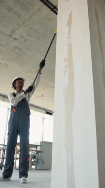 Profesyonel müteahhit, inşaat halindeki bir binanın içindeki büyük bir duvara alçı uygulamak için uzun bir silindir kullanıyor ve tamamlama sürecinde önemli bir adım atıyor.