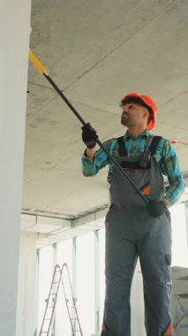 Dairenin yenilenmesi sırasında iç duvarlara ve tavanlara beyaz astar takan üniformalı profesyonel bir ressam, inşaat endüstrisinin iş becerilerini ve güvenlik uygulamalarını gösteriyor