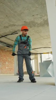 Koruyucu turuncu şapka takan inşaat işçisi, tamamlanmamış ticari ofis yenileme projesinde çalışırken uzun fırçalı astarı dikkatlice uyguluyor.