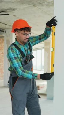 Üniformalı ve şapkalı profesyonel inşaat işçisi inşaat projesi sırasında duvarın dikey hizasını dikkatlice kontrol ederek, ruhsal düzeyi ile hassasiyet ve doğruluğu sağlıyordu.