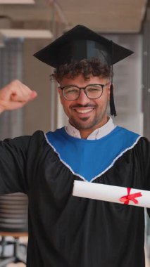 Akademik önlük ve havan panosu giyen heyecanlı mezun, mezuniyeti diplomasını atarak ve üniversite binasında zafer kazanarak kutluyor.