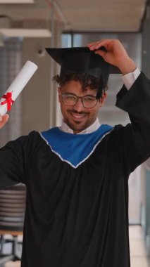 Mezuniyet elbisesi giyip diplomasını tutan, havan topunu fırlatan ve baş parmağını kaldıran mutlu bir mezunun görüntüsü.