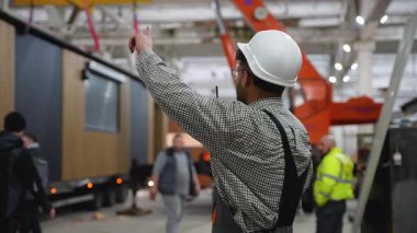 Mühendis telsiz ve el işaretleriyle iletişim kuruyor. Büyük bir sanayi fabrikasının içindeki prefabrik ev modülünün taşınmasını koordine ediyor.