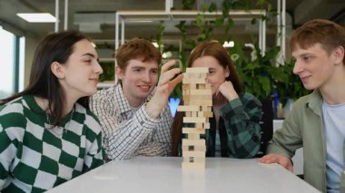 Beyaz masanın etrafında toplanan Kafkasyalı genç arkadaşlar, artan gerilimle jenga oynuyorlar, rekabetçi grup etkileşiminde ahşap blokları dengelerken konsantre ifadeler sergiliyorlar.