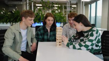 Kafkasyalı öğrenciler canlı bir Jenga oyunundan hoşlanırlar, tahta kuleden blokları dikkatlice kaldırırlar, ifadeleri odaklanmış konsantrasyondan oyuncu beklentisine kadar değişir.