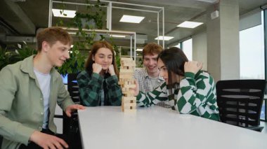 Kafkasyalı genç yetişkin öğrenciler, çağdaş ofis ortamında popüler bir blok istifleme oyunu olan jenga oynayarak boş zamanlarının tadını çıkarıyorlar.