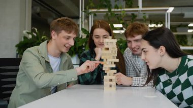 Kafkasyalı genç öğrenciler Jenga oynamaya odaklandılar, dikkatle bir kuleden tahta blokları kaldırdılar, ve sonra kule düştüğünde onların komik tepkileri