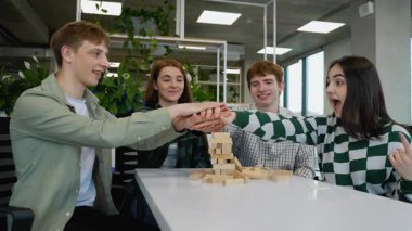 Kafkasyalı genç yetişkin öğrenciler, boş zamanlarında Jenga oynayarak, dikkatle istifleyerek ve bir ofis dinlenme odasında tahta blokları dengeleyerek eğleniyorlar.