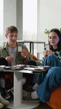 İki neşeli genç, turuncu puf minderlerde dinleniyor, masa başında oyun oynuyorlar, görünür bir heyecan ve neşe ile oynuyorlar ve kapalı alanda birlikte kaliteli zaman geçiriyorlar.