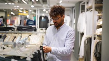 Genç erkek müşteri yeşil pantolonları dikkatle inceliyor, modern perakende piyasasında düşünceli seçim sürecini sergiliyor, moda bilinci ile odaklanmış alışveriş yaklaşımını somutlaştırıyor