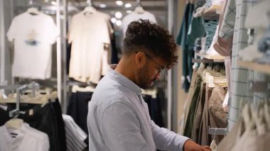 Çağdaş giyim mağazasında alışveriş yaparken erkek müşteriler dikkatli bir şekilde gömlekleri ve pantolonları inceliyor ve kişisel kıyafet seçimi için farklı giyim seçenekleri düşünüyorlar.