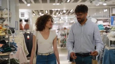 Neşeli ortaklar elbise raflarına göz gezdiriyorlar, alışveriş torbaları taşıyorlar ve canlı sohbetler yapıyorlar. Bu arada, modern, parlak mağaza içinde perakende alışveriş deneyimlerinin tadını çıkarıyorlar.