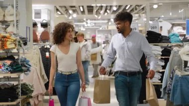 Neşeli çiftler iç mekanlara göz gezdirirken, alışveriş torbaları taşırken, gülümserken, konuşurken ve ortak alışveriş deneyimlerinden zevk alırken.