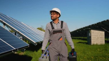 Profesyonel araçlar taşıyan bakım mühendisi, sürdürülebilir enerji teknolojisi ve yenilikçi işyeri uygulamalarını temsil eden güneş ışığıyla aydınlanan fotovoltaik santralde güvenle yürüyor