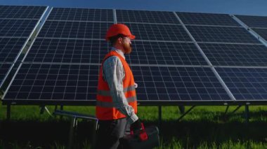 Kızıl başlı profesyonel mühendis güneş paneli altyapısını koruyor, güneş ışığında araçları ve merdiveni taşıyor, sürdürülebilir enerji teknolojisini ve temiz enerji üretimini somutlaştırıyor