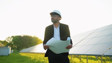 Güvenlik kaskı takan profesyonel mühendis, kırsal bir ortamda bir güneş paneli kurulumunu değerlendirirken, verimli ve sürdürülebilir enerji üretimini sağlarken, projeleri gözden geçiriyor