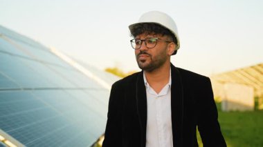 Altın gün batımında fotovoltaik güneş çiftliğini denetleyen koruyucu başlık takan profesyonel mühendis sürdürülebilir teknoloji ve yeşil enerji gelişimini temsil ediyor.