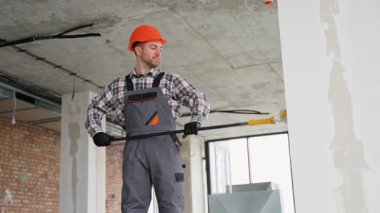 Güvenlik kaskı ve iş tulumu giyen profesyonel müteahhit, inşaat halindeki bir binanın alçı tavanını incelemek için teleskopik bir araç kullanıyor.