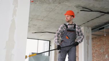 Üniforma giyen profesyonel bir ressam, inşaat halindeki bir binanın geniş yüzeyini kaplamak için teleskopik boya silindiri kullanır.