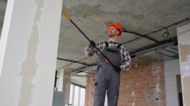 Turuncu kasklı ve gri üniformalı inşaat işçisi inşaat halindeki bir binanın tavanını kontrol etmek için teleskopik kontrol aynası kullanıyor.