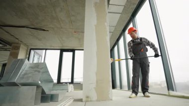 Profesyonel ressam, modern inşaat alanındaki yenileme işlemleri sırasında uzun silindirleri kullanarak, büyük iç duvarlara dikkatlice astar katmanı uyguluyor.