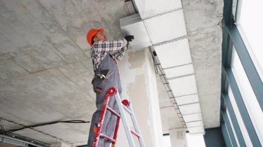 Tulumlu ve eldivenli teknisyen havalandırma kanalı kurulumunda çalışıyor..