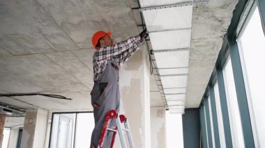 Üniformalı ve eldivenli havalandırma teknisyeni modern ofis binasının tavanında havalandırma sistemi kuruyor ya da onarıyor.