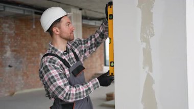 Üniforma giyen profesyonel müteahhit inşaat veya yenileme sırasında duvarın dikey düzlüğünü kontrol etmek için ruh seviyesini kullanır