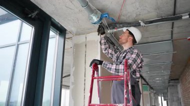 Profesyonel tesisatçı, inşaat halindeki bir binanın içindeki boru hattı bağlantılarını titizlikle denetliyor ve ayarlıyor.