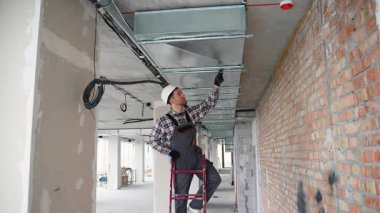 Teknik üniformalı deneyimli işçiler, temiz hava ve uygun hava akışı yönetimi sağlamak amacıyla modern bir ofise tavandan monte edilmiş havalandırma sistemi kuruyor..