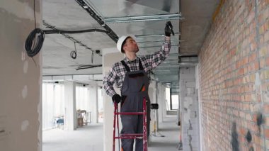 Üniformalı profesyonel teknisyen ofis tavanında havalandırma sistemi kuruyor, iç hava kalitesini arttırıyor ve modern iklim kontrolünü sağlıyor.