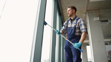Modern ofis binasının pencerelerini dikkatlice temizleyen erkek profesyonel temizlikçi teleskobik cam ve mavi koruyucu eldivenler kullanarak el değmemiş cam yüzeyleri koruyor.