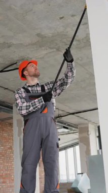 Üniforma giyen profesyonel müteahhit teleskopik bir teftiş aynası tutuyor ve inşaat halindeki bir binanın tavanını dikkatlice inceliyor.