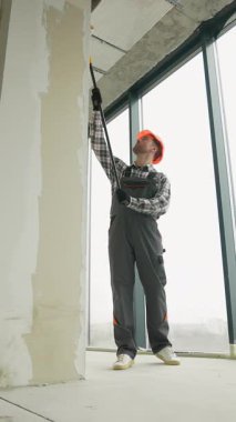 Gri üniformalı profesyonel bir ressam ve turuncu kasklı dikkatli bir şekilde duvarlara astar takıyor. Yeni apartman dairesini son resim sahnesi için hazırlıyor.