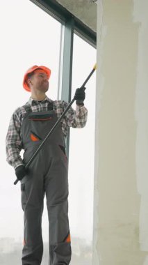 Profesyonel pencere temizleyicisi koruyucu üniforma giyiyor ve uzun saplı fırça ve şehir manzaralı deterjan kullanarak büyük cam pencereleri temizliyor.