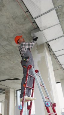 İş üniformalı yetenekli teknisyenler modern ofis tavanına havalandırma kanalları kurarak hava dolaşımını ve bina standartlarına uymayı sağlıyorlar..