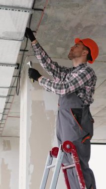 Üniformalı profesyonel teknisyen ofis tavanında havalandırma sistemi kuruyor, iç hava kalitesini arttırıyor ve modern iklim kontrolünü sağlıyor.