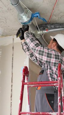 Profesyonel tesisatçı, inşaat halindeki bir binanın içindeki boru hattı bağlantılarını titizlikle denetliyor ve ayarlıyor.