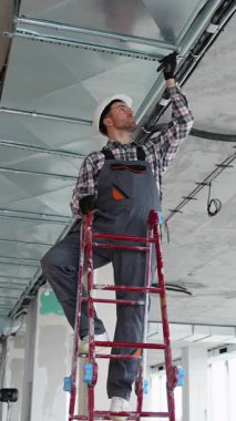 Üniformalı ve eldivenli havalandırma teknisyeni modern ofis binasının tavanında havalandırma sistemi kuruyor ya da onarıyor..