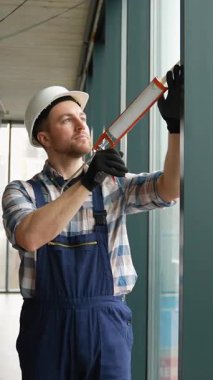 Kaliteli inşaat işçisi koruyucu ekipman giyer titizlikle pencere çerçevesini kapatır, su geçirmez ve hava geçirmez profesyonel sınıf kurulumuna odaklanır.