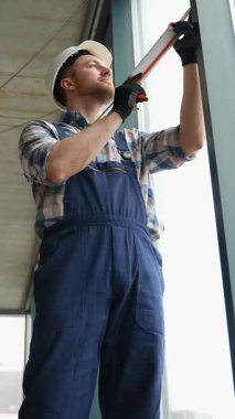 Profesyonel inşaatçı, hassas kurulum sırasında pencere çerçevesini dikkatlice indiren, güvenlik donanımı takan ve modern inşaat projesinde doğru hizalamayı sağlayan